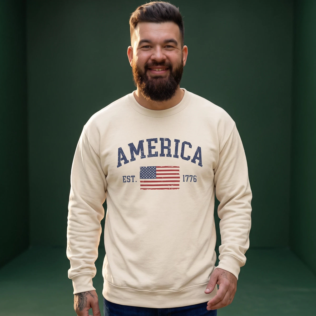 A man wearing a Crown N Thread cream crewneck sweatshirt with a vintage America 1776 flag graphic on the chest.