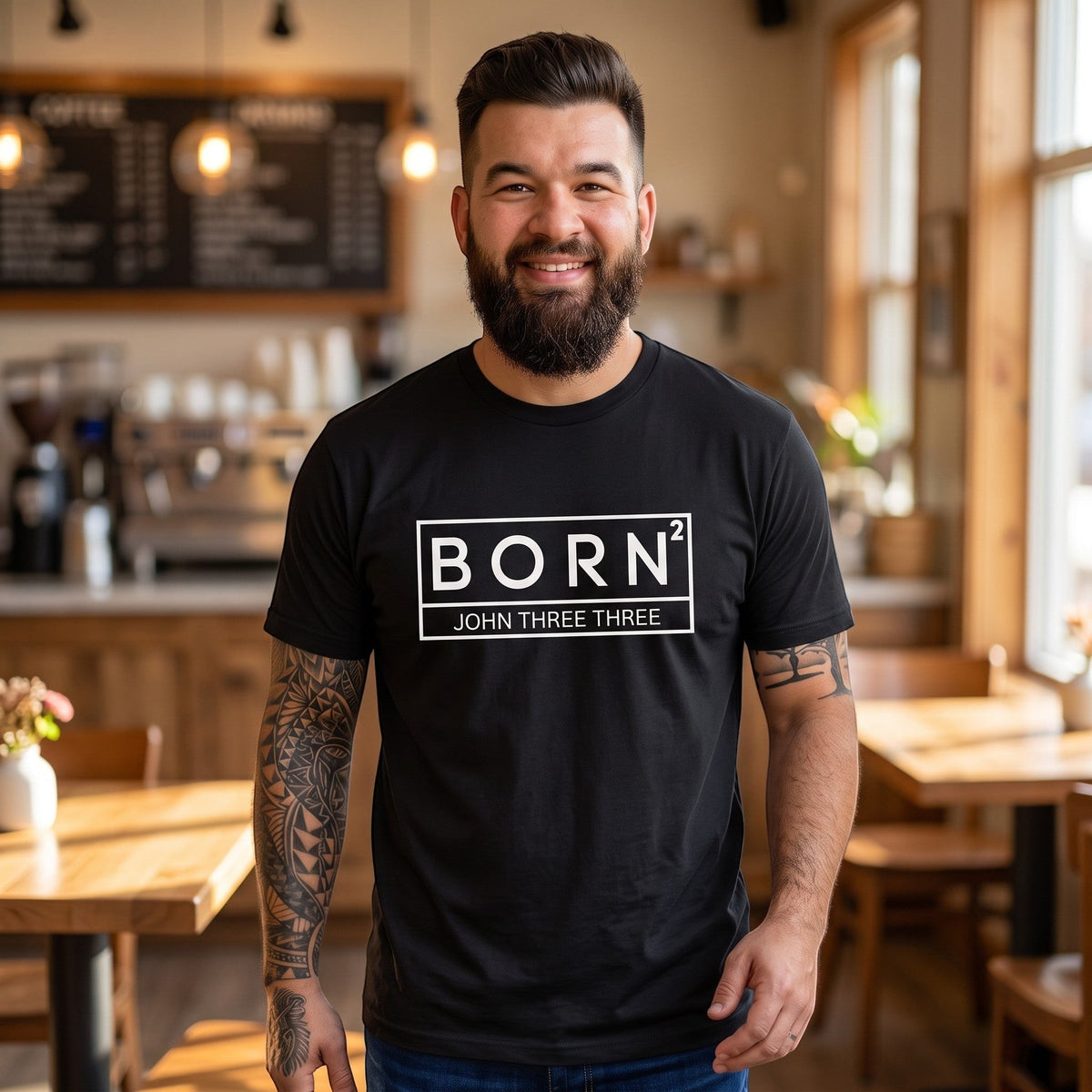 A smiling man wearing a black Crown N Thread cotton graphic tee with a white BORN2 John Three Three logo in a cafe.