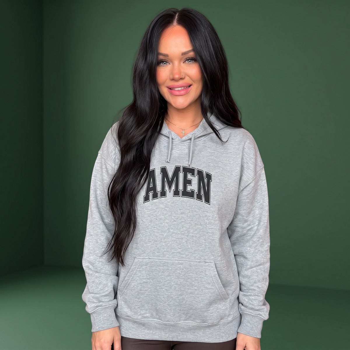 A woman wearing a Crown N Thread grey cotton-poly hoodie with AMEN in black collegiate script on a green background.