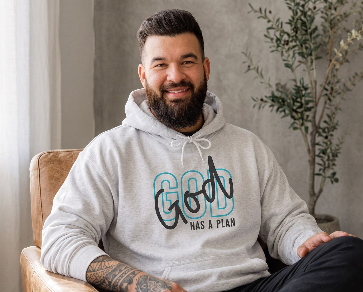 A bearded man wearing a Crown N Thread heather grey pullover hoodie with God Has a Plan graphic, sitting in a chair.