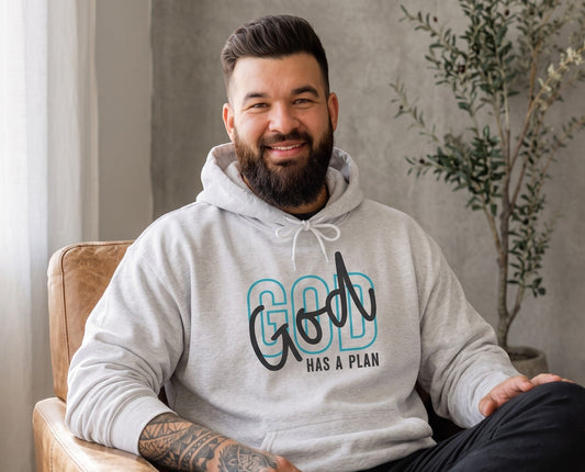 A bearded man wearing a Crown N Thread heather grey pullover hoodie with God Has a Plan graphic, sitting in a chair.
