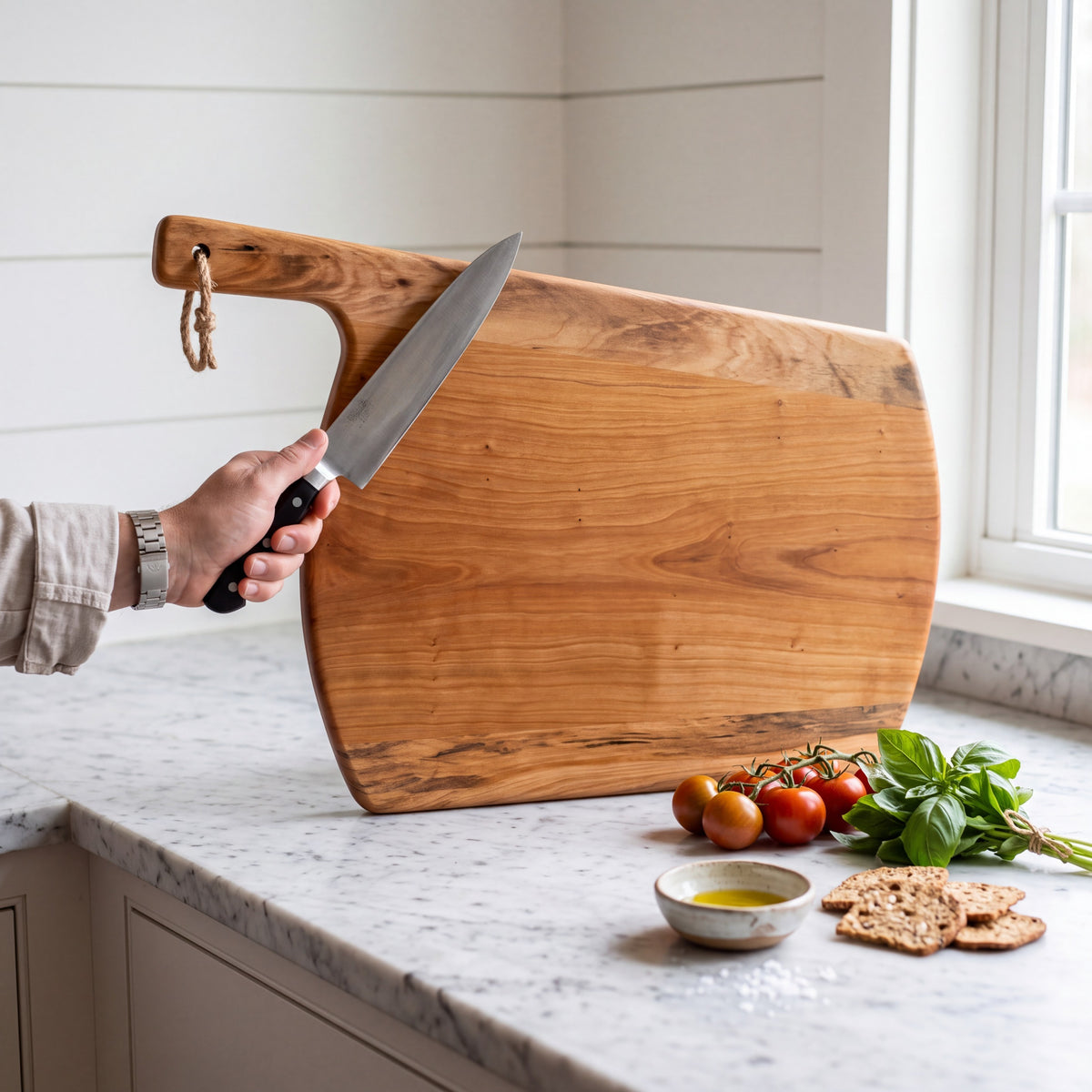 Crown N Thread handmade oiled wood charcuterie board with a handle, held by a hand with a knife on a marble counter.