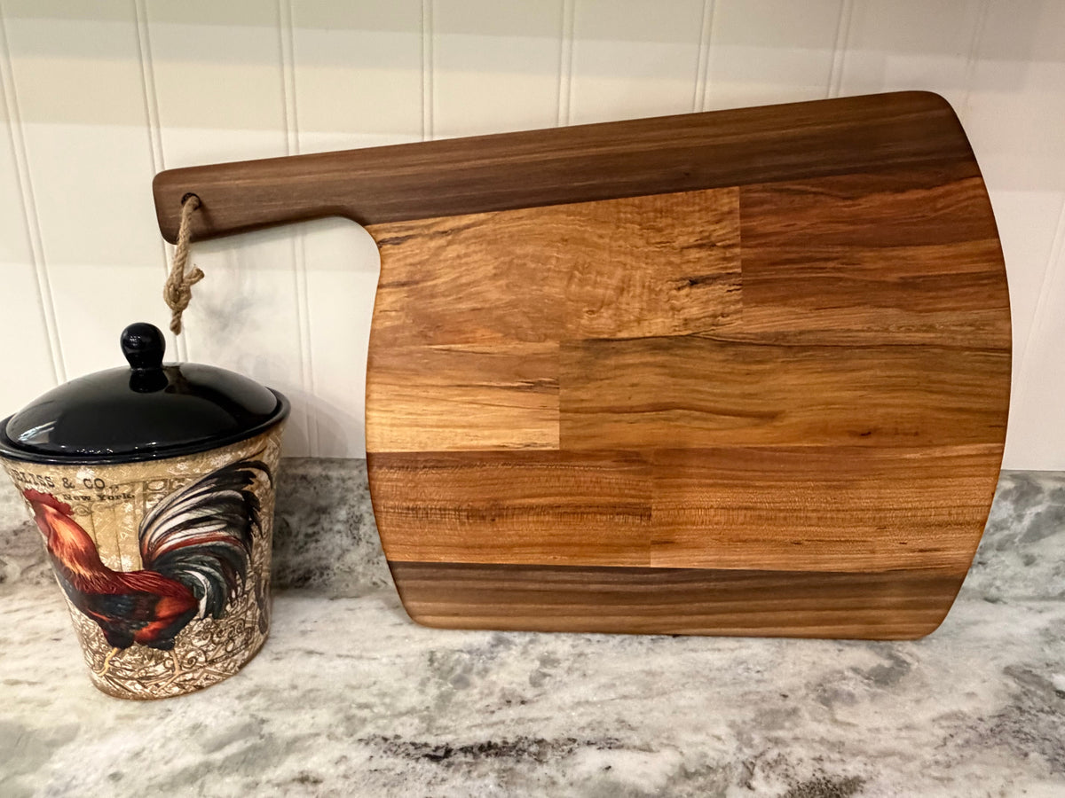 Crown N Thread handmade oiled wood charcuterie board with a rustic rope handle, displayed on a kitchen countertop.